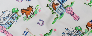 Cartoon horses, barns, pink award ribbons, fences, and horseshoes are scattered across a white fabric with a playful, hand-painted design.