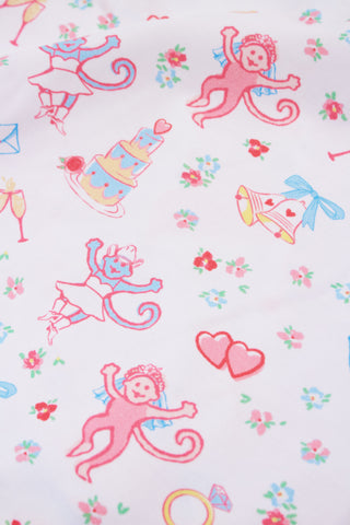 Colorful pattern on white fabric featuring cartoon monkeys in tutus, cakes, hearts, flowers, rings, champagne glasses, and love letters, creating a playful, romantic theme.