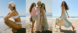 Three women pose on a sunny beach in light, floral-patterned summer outfits—bikinis, dresses, and hats—one squatting, two standing with shoes in hand, and one walking with a woven tote.