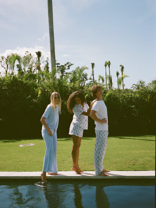 Three people standing by a pool with a scenic background of trees and sky.