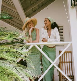 Two women standing on a porch with palm leaves in the foreground