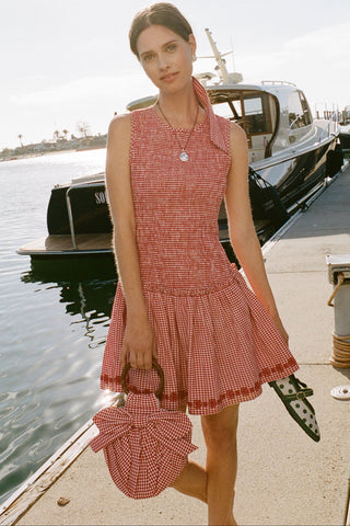 Woman in a red checkered dress standing on a dock with boats in the background