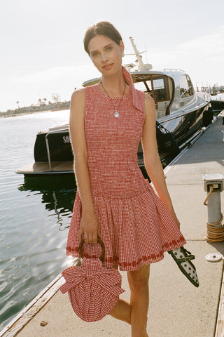 Woman in a red checkered dress standing on a dock with boats in the background