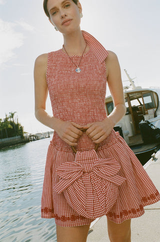 The Roller Rabbit Gingham Miranda Purse features red gingham fabric, a large red and white bow, gathered detailing, and a round bracelet handle, shown against a plain white background.