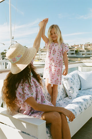 A woman and girl in Roller Rabbit floral dresses sitting on a white couch with a scenic background.