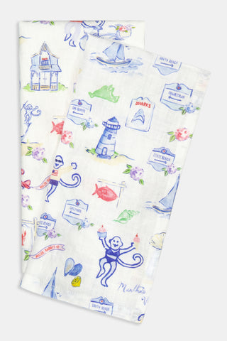 Two white cloth napkins featuring colorful, whimsical illustrations of beach scenes, lighthouses, monkeys, sea animals, houses, and signs labeled with various beach names—all in a charming hand-drawn style.