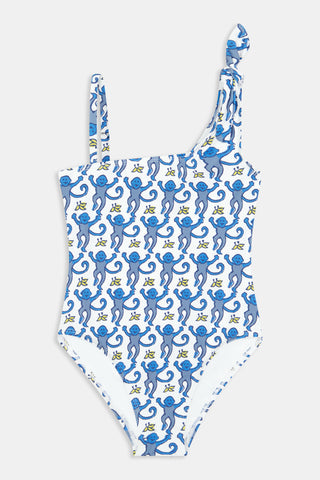 The Monkey Kids Jacey One Piece by Roller Rabbit is a white, one-shoulder swimsuit with blue monkeys and yellow bananas. It features an asymmetrical neckline, a knotted right tie strap, and playful monkey illustrations.