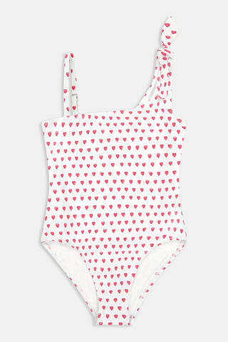 The Roller Rabbit Hearts Kids Jacey One Piece is a swimsuit with an asymmetrical neckline, white fabric dotted with pink hearts, and an adjustable knot-tied shoulder strap.