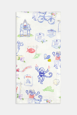 Set of four white Ecovero linen napkins by Roller Rabbit, featuring whimsical, cartoon-like beach-themed illustrations—monkeys, sailboats, houses, bicycles, and seashells—in vibrant blue, red, green, and purple hues. Made in India. Product name: Monkey On The Vineyard Napkin Set Of 4.