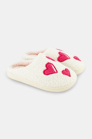 Kids Hearts Fuzzy Slippers: a pair of cream-colored fuzzy kids slippers decorated with red heart appliques.