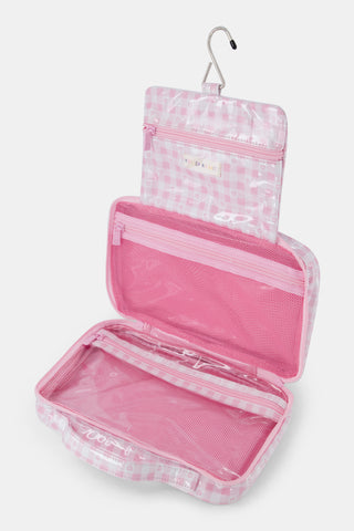 The Roller Rabbit Gingham Hearts Hanging Toiletry Case is a rectangular travel bag featuring pink and white gingham checks adorned with small heart patterns and a top handle, displayed against a plain white background.