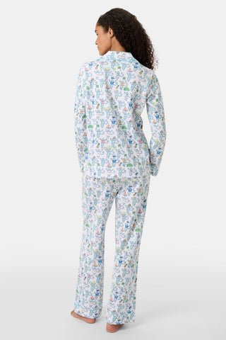 A person with curly hair stands barefoot, facing away, wearing the Charleston Monkey Long Sleeve Polo Pajamas—Pima cotton pajamas featuring a relaxed-fit top and pants with a colorful botanical and animal print on white.