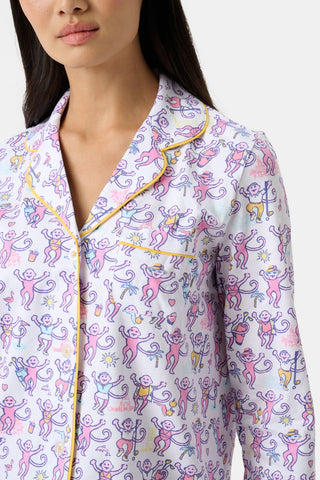 A woman wears Palm Beach Monkey Long Sleeve Polo Pajamas, made from soft Pima cotton with a vibrant pink and purple monkey print, yellow piping at the collar and lapel, and a front pocket.