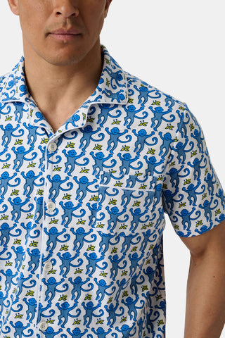 A man models the Mens Monkey Louie Pajamas short-sleeved button-up shirt, crafted from 100% Pima cotton with a playful blue monkey print on a white background, shown from shoulders to waist against a plain backdrop.