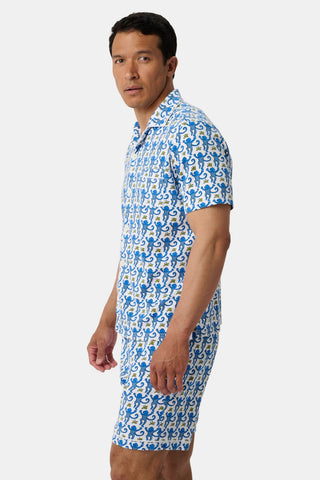 Man standing sideways, wearing Mens Monkey Louie Pajamas—a matching short-sleeve shirt and shorts with blue and white cartoon-style cat print, made from 100% Pima cotton—against a plain white background.