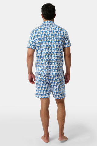 A man stands barefoot, facing away, modeling the Mens Monkey Louie Pajamas—a matching blue and white short-sleeve button-up shirt and shorts set with an all-over seahorse print in 100% Pima cotton—against a plain white background.