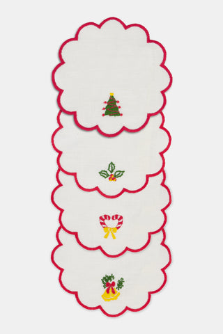 Seasons Soiree Scallop Cocktail Napkin Set Of 4: four round 100 linen napkins with scalloped red edges, each featuring a different embroidered Christmas icon: a tree, holly, a candy cane, and bells.