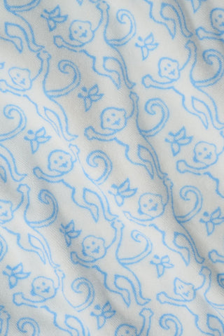 A young child smiles at the camera while wearing the Roller Rabbit Kids Monkey Jesse Cover Up, a light blue and white terry zip-up onesie with a playful animal pattern, against a plain background.