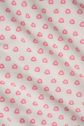 A young girl with long brown hair wears the Roller Rabbit Kids Hearts Jesse Cover Up, a white hooded zip-up towel robe with pink hearts and front pockets, smiling at the camera against a plain light background.