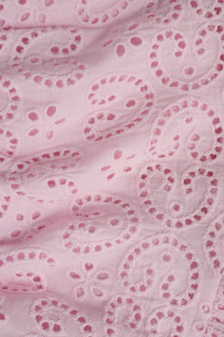 Close-up of light pink fabric from the Kids Clover Eyelet Emry Skirt by Roller Rabbit, highlighting embroidered paisley patterns with small circular cutouts and stitched outlines on a slightly textured surface.