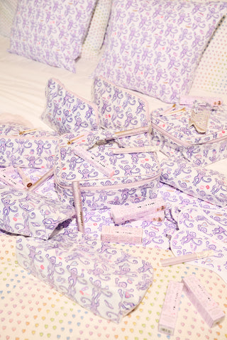 Introducing the STREET SMART Get Ready With Me Makeup Bag, featuring a whimsical white design adorned with playful purple monkeys holding bananas, lipstick, and shoes, surrounded by scattered lips and compact mirrors on a clean background.