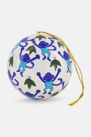 Round white hand-painted Monkey Ornament by Roller Rabbit featuring a repeating pattern of blue monkeys and green leaves, hanging from a gold string.