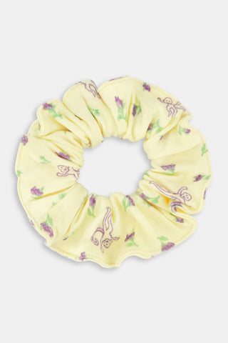 The Roller Rabbit Mini Monkey Blossom Scrunchie is a yellow 100 cotton hair accessory featuring a ruffled design, adorned with small purple flowers and playful purple monkey illustrations.
