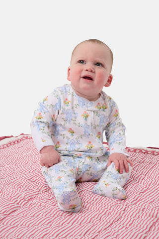 Baby wearing a floral onesie sitting on a pink and white striped blanket.
