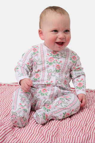 A light-skinned, dark-haired baby sits outdoors on a blue and white blanket, wearing Roller Rabbit Infant Monkey Block Stripe Zipper Footie, with green grass and bushes in the background.