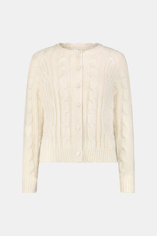 The Ruby Cardigan by REVOLUTION KNITS is a cream-colored, alpaca blend cable-knit cardigan with a crew neck and button front, worn over a red and white patterned skirt.