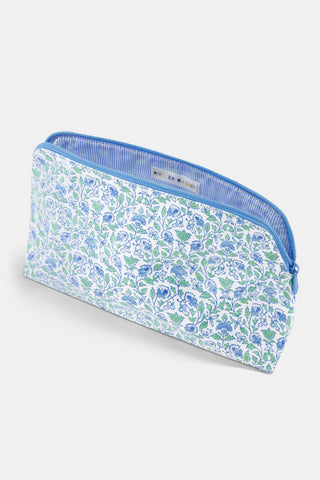 The Roller Rabbit Garden Gate Floral Makeup Bag features a rectangular zippered design with a blue and green floral pattern on a white cotton canvas background, photographed against a simple light backdrop. Perfect for organizing your beauty essentials at home or while traveling.