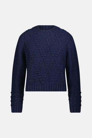A person wearing a navy blue REVOLUTION KNITS Popcorn Knit Tessa Sweater featuring a textured, popcorn-stitch diamond pattern and a mock-neck.