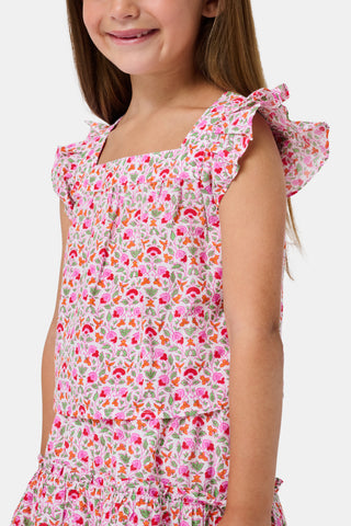 Three young girls sit close together outdoors, each wearing the Roller Rabbit Kids Garden Gate Floral Emmett Top—an ideal choice for girls' summer clothing. They are smiling and appear to be engaged in conversation, with greenery and stone walls in the background.