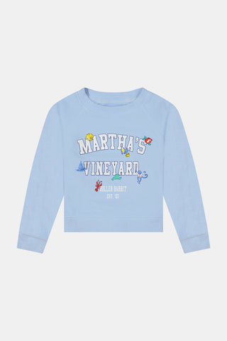 A young girl wears the Kids MV Icons Crewneck by Roller Rabbit—a blue fleece top adorned with playful illustrations—paired with a white skirt featuring colorful prints, standing against a plain background.