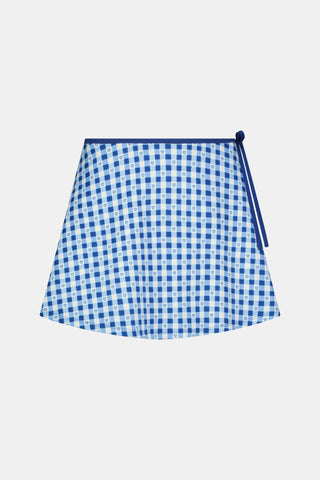 Wearing the Roller Rabbit Gingham Hearts Coco Wrap Skirt, a woman stands next to a net outdoors, surrounded by green grass and trees.