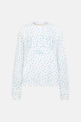 A person wearing a white Roller Rabbit Mini Monkey Blossom Andie Sweatshirt, featuring small blue and green Mini Monkey Blossom prints and large SLEEP Club lettering, stands outdoors, partially in sunlight. Their face is mostly out of frame.