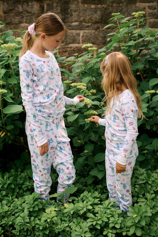 The Kids Game Day Pajamas by Roller Rabbit are a children’s long-sleeve pajama set crafted from soft Pima cotton, featuring a vibrant party-themed print with colorful dinosaurs, bunting, gifts, and party hats on a white background.