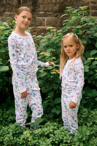 The Kids Game Day Pajamas by Roller Rabbit are a children’s long-sleeve pajama set crafted from soft Pima cotton, featuring a vibrant party-themed print with colorful dinosaurs, bunting, gifts, and party hats on a white background.