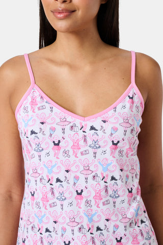 A woman wearing the Roller Rabbit Monkey Pirouette Mischa Set—pink and white cat-print Pima cotton loungewear—and holding a matching bag stands in front of white lockers, smiling slightly at the camera.