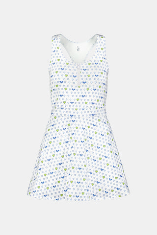 The Roller Rabbit Tennis Hearts Becky Active Dress is a sleeveless white active dress with a V-neckline and a flared skirt, adorned with an all-over pattern of small blue and green heart shapes. The dress is shown against a plain light gray background.