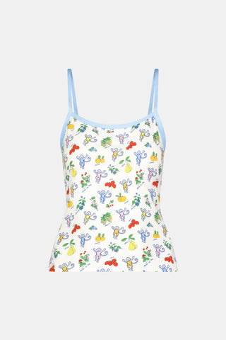 A woman wears the Monkey Fruits D’Ete Clarkson Cami by Roller Rabbit, a sleeveless white cotton-modal cami with light blue trim and a colorful fruit and cartoon print. The matching bottoms are partially visible against a plain white background.
