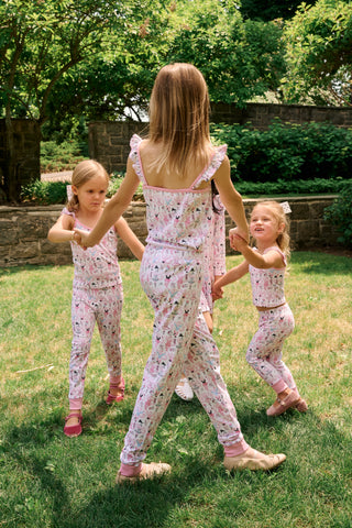 The Kids Monkey Pirouette Blaire Pajamas by Roller Rabbit is a children's pajama set crafted from soft Pima cotton, featuring a sleeveless top with ruffled straps and long pants, both in white with a playful pink, blue, and black monkey cartoon print and pink trim.