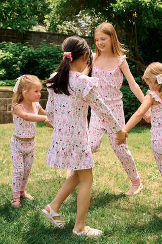 The Roller Rabbit Kids Monkey Pirouette Isa Dress features long sleeves, a pink collar, and ruffle shoulders. Crafted from soft Pima Cotton for all-day comfort, this dress showcases a playful pattern of cartoon monkeys dancing pirouettes on a white background.