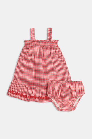 A young girl in the Roller Rabbit Kids Gingham Teagan Dress with an embroidered hem stands barefoot on a boat deck by the water, sunlight shimmering on the surface.