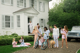 Family gathering in front of a white house with a car and dog present.