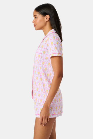 Introducing the Monkey Fiora Pajamas from Roller Rabbit—crafted from fabric adorned with a delightful pattern of pink and yellow monkeys with curled tails and smiling faces, interspersed with tiny leaves on a crisp white background. Perfect for adding playful charm to your sleepwear collection.