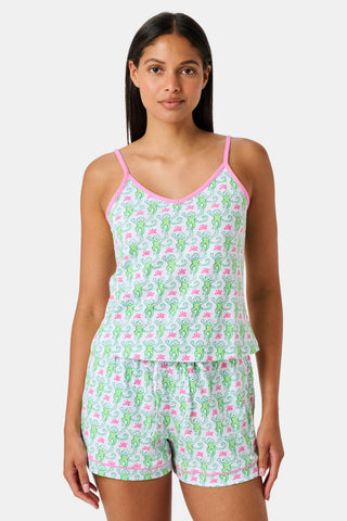 A woman wearing the SERFLEX Monkey Mischa Set, a coordinated sleeveless top and shorts with pink straps and a fun pink and green flamingo print, made from soft Pima cotton, stands against a plain white background.