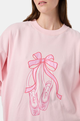 A person with long blonde hair in a ballet slipper-pink Roller Rabbit Monkey Pirouette Andie Sweatshirt holds patterned folders in front of white lockers.