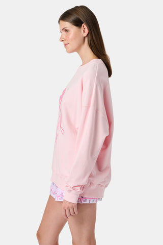 A person with long blonde hair in a ballet slipper-pink Roller Rabbit Monkey Pirouette Andie Sweatshirt holds patterned folders in front of white lockers.
