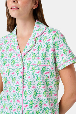 A woman wearing the Roller Rabbit Monkey Polo Pajamas, a short-sleeve button-up set with matching shorts featuring a green and pink floral pattern, stands against a plain white background.
